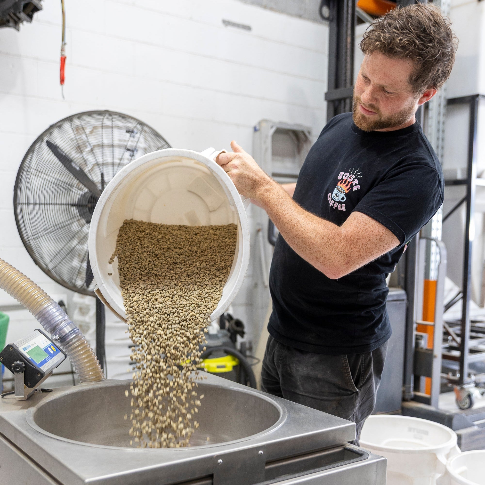 Person transferring coffee beans from a container into a machine in a warehouse setting.